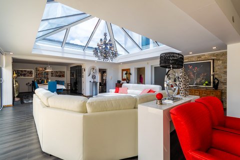 Sala de estar ampla, claraboia, sofá branco e cadeira vermelha.
